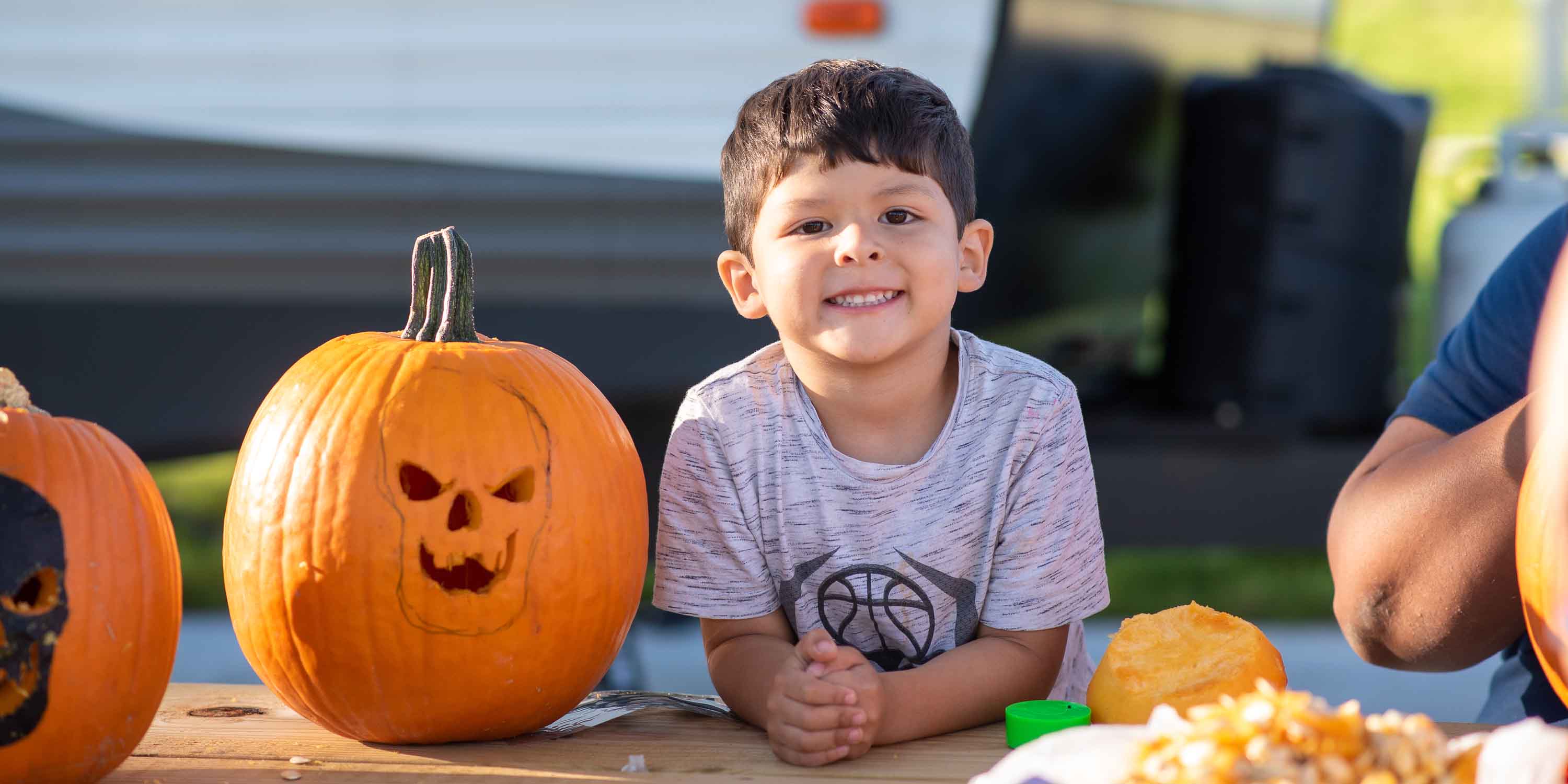 A child smiling next to his carved pumpkin at Camp Fimfo during Halloween Weekends