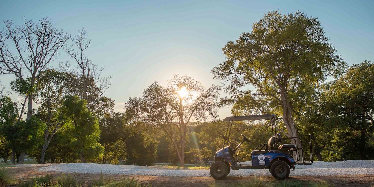 A golf cart parked along a trail covered in spring greenery at Camp Fimfo Texas Hill Country