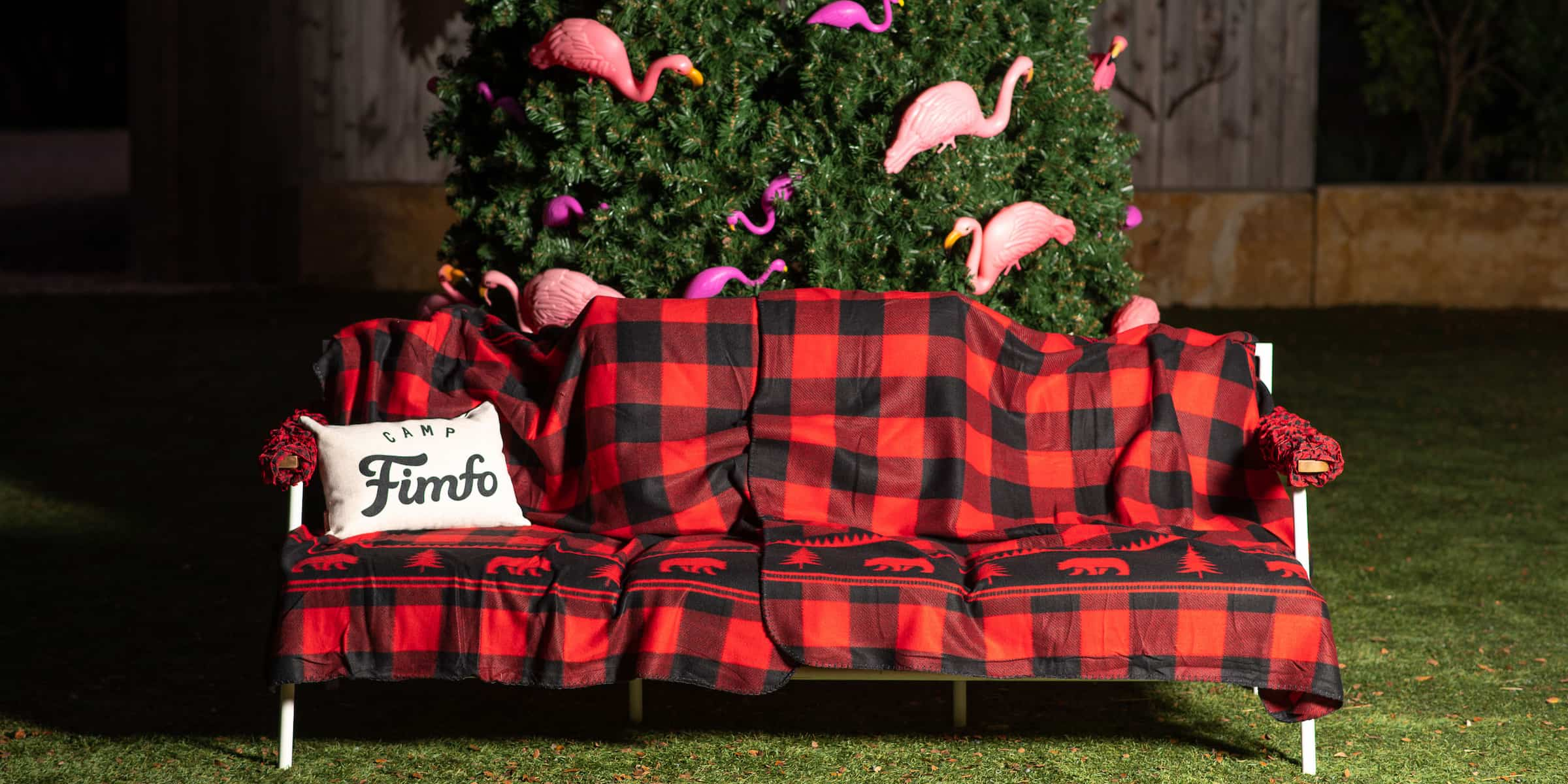 A holiday inspired blanket and Camp Fimfo pillow laid on a bench in front of a fun Christmas tree.