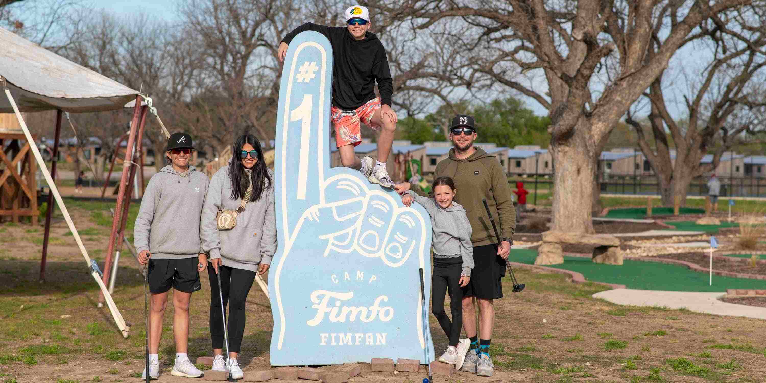 A family posing next to the Camp Fimfo Waco foam finger that says "Camp Fimfo Fimfan"