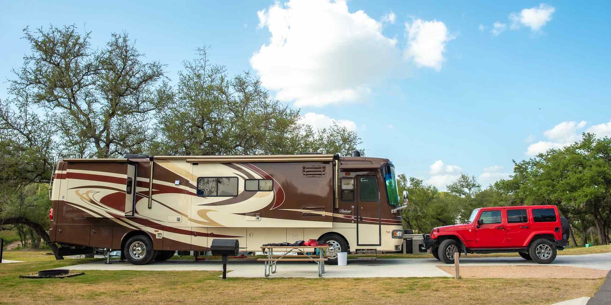 An RV site with a motorhome and a car at Camp Fimfo