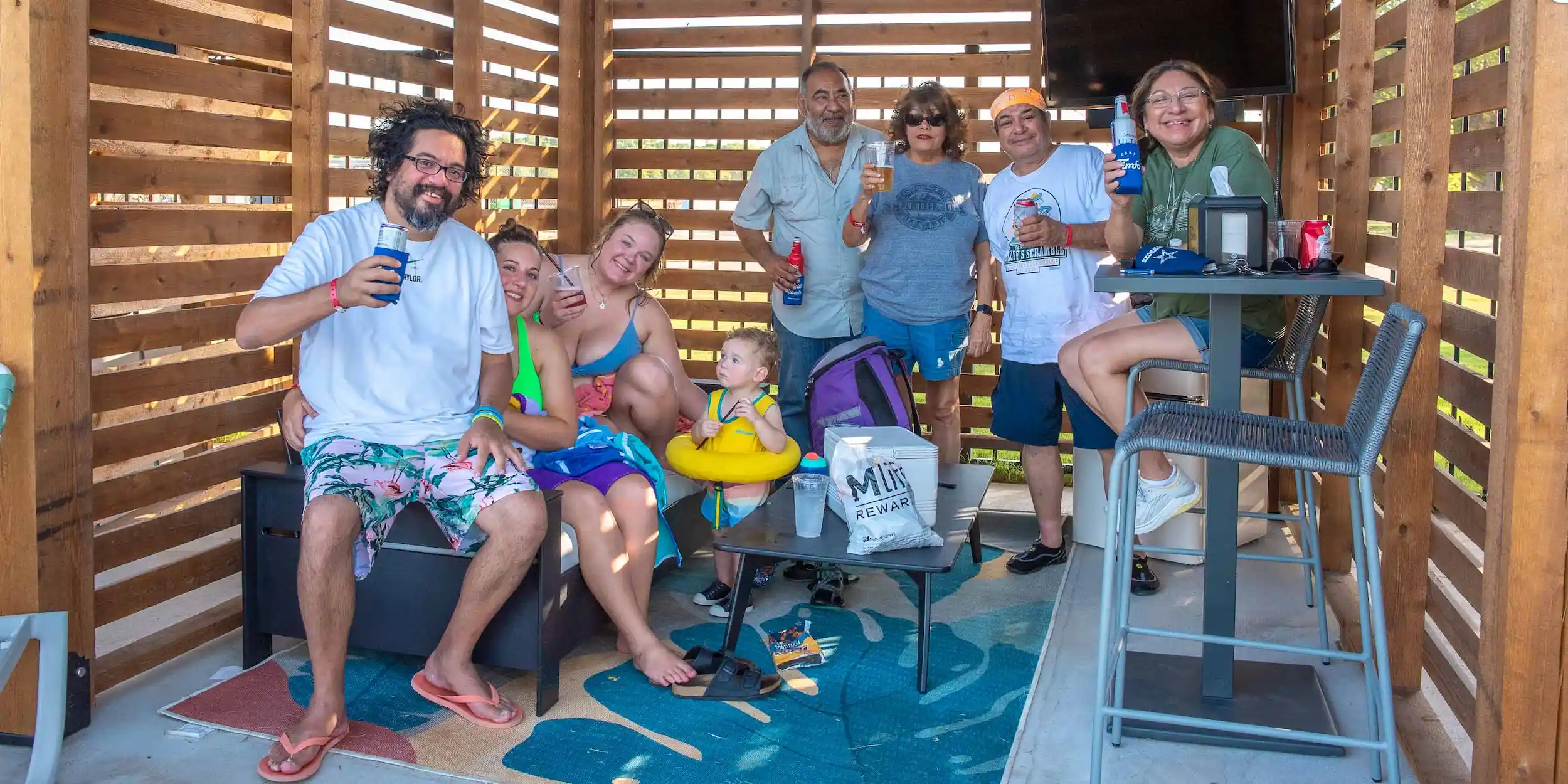 A group of guests at Camp Fimfo Waco, smiling and holding drinks in a private poolside cabana