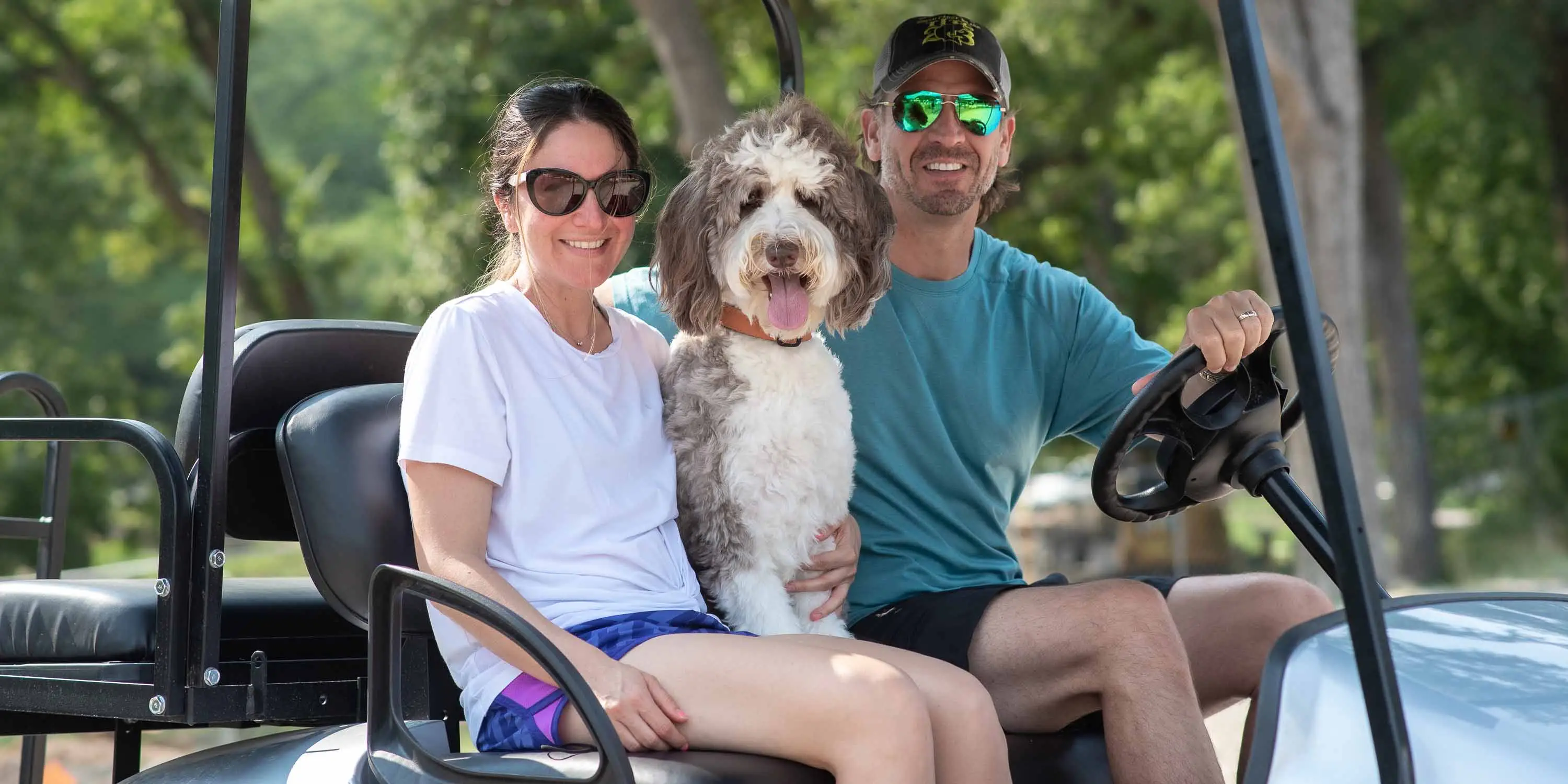 A couple smiling on a golf cart with their dog at Camp Fimfo 