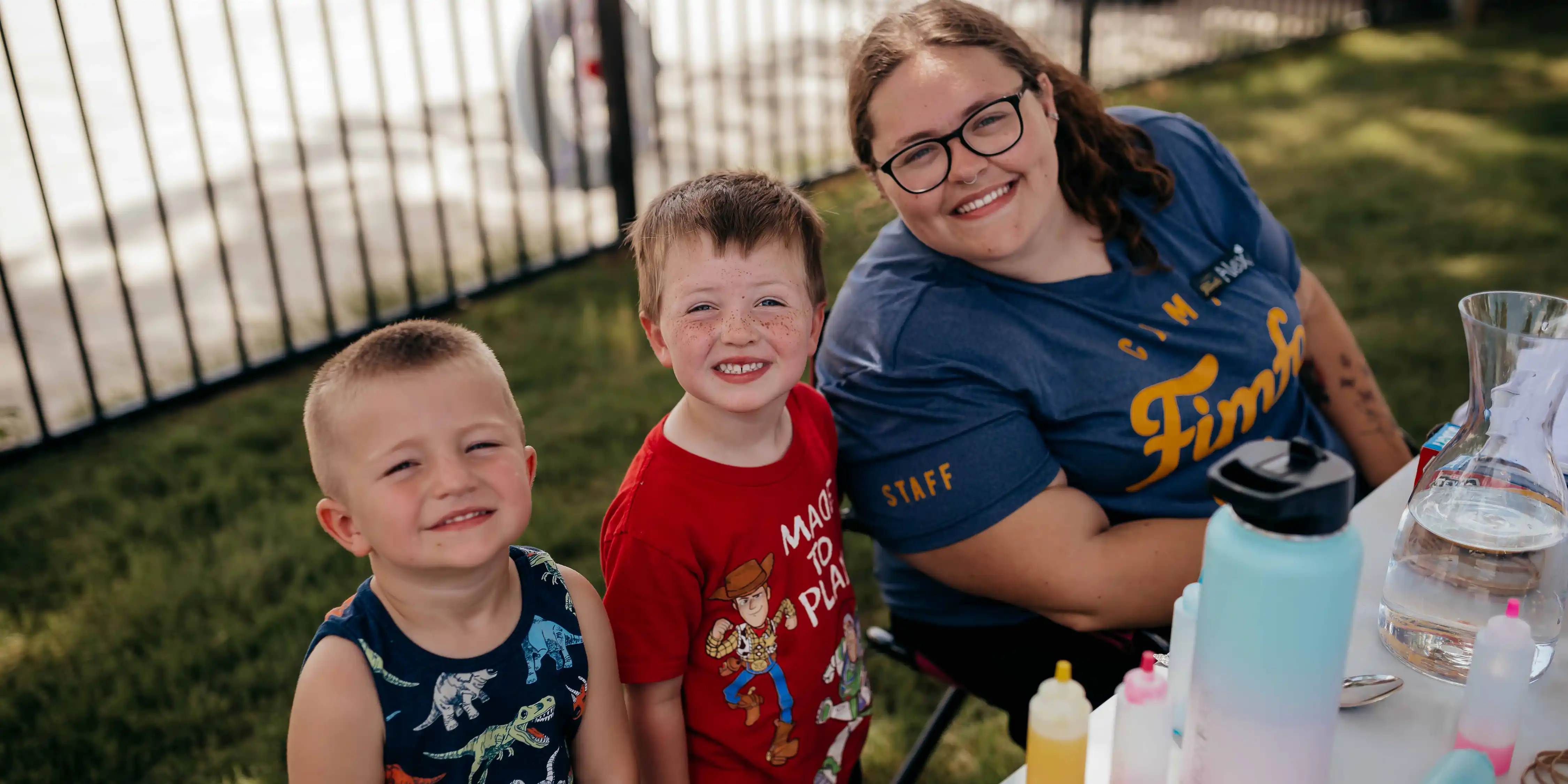 A smiling Camp Fimfo staff member sitting next to two smiling children during a tie dye event