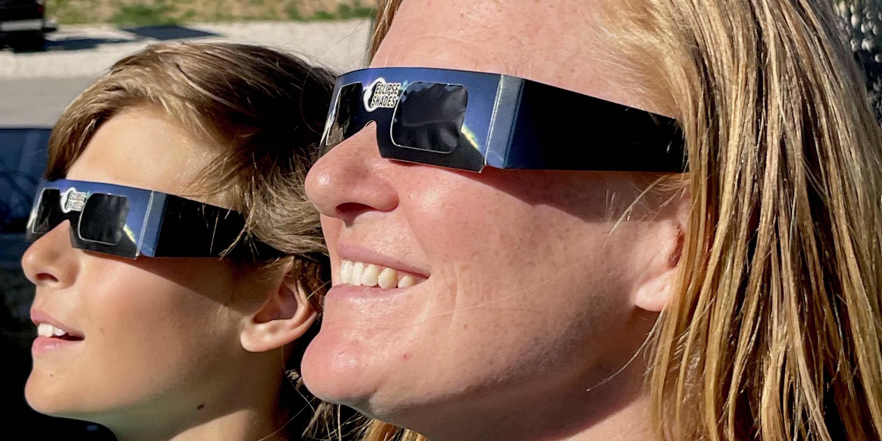 Two people wearing eclipse glasses and looking up at the sky