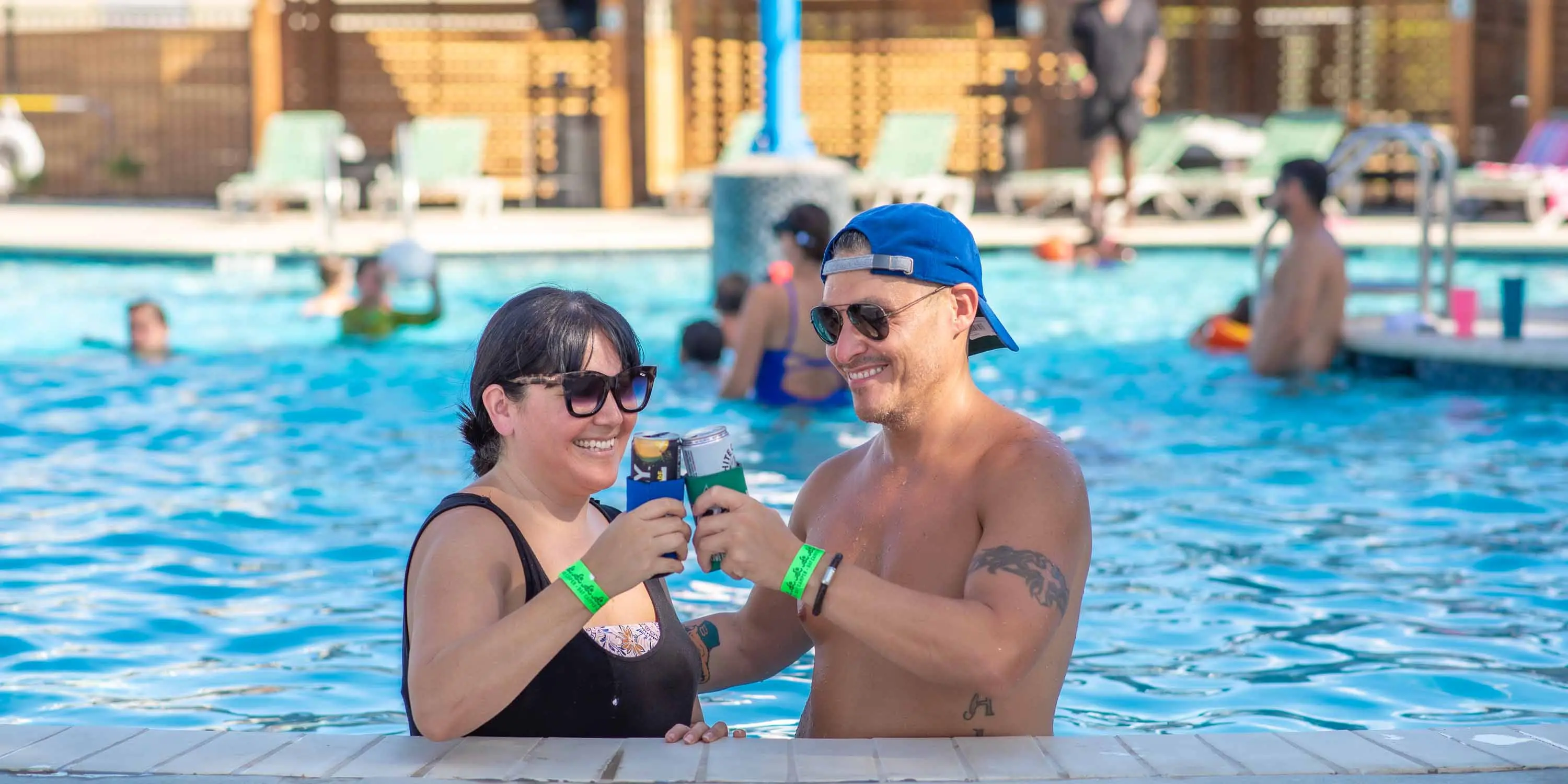 A couple standing in the Camp Fimfo Waco resort-style pool with drinks from the swim-up bar