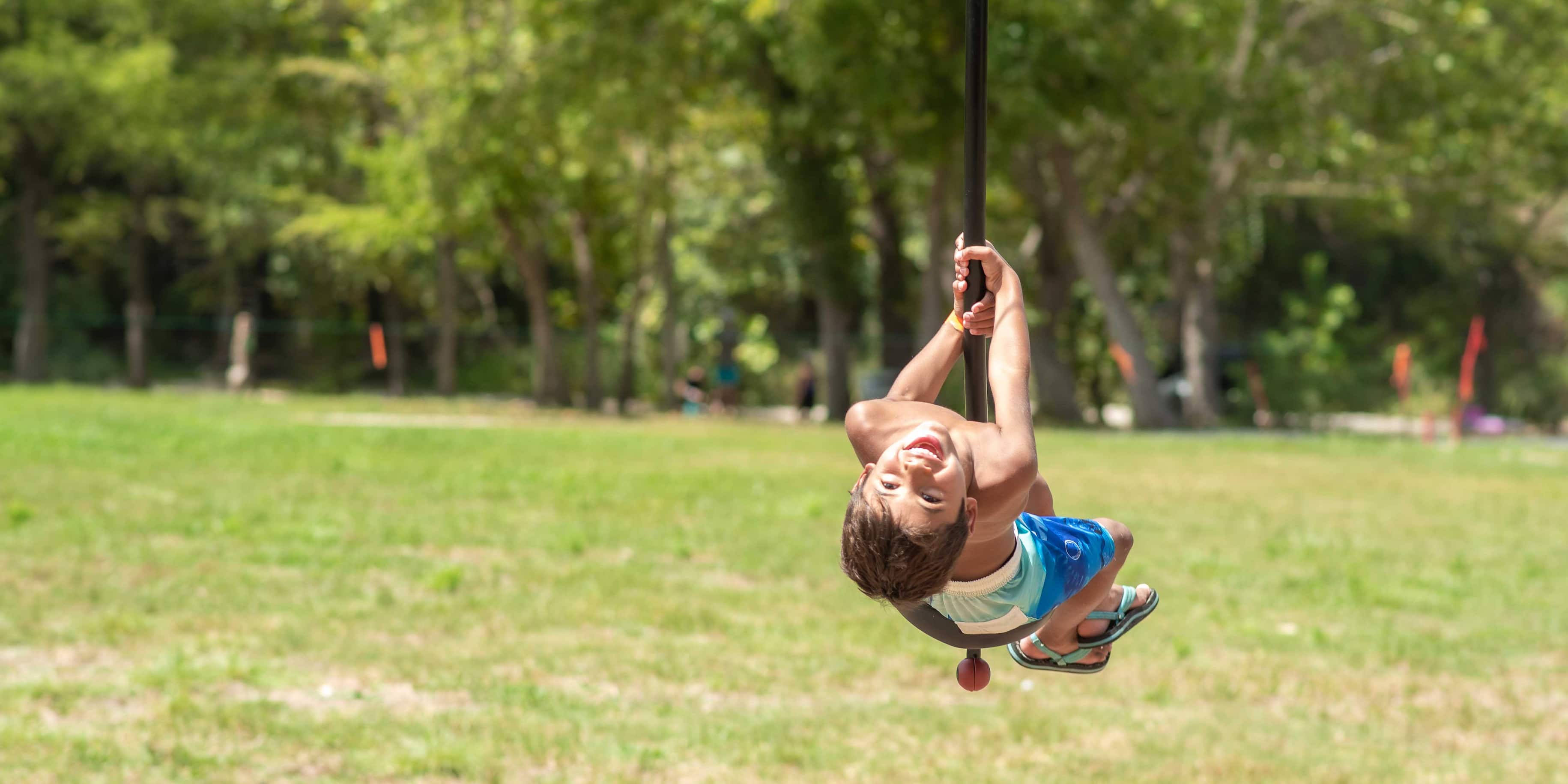 A smiling young child riding the playground zipline at Camp Fimfo Texas Hill Country