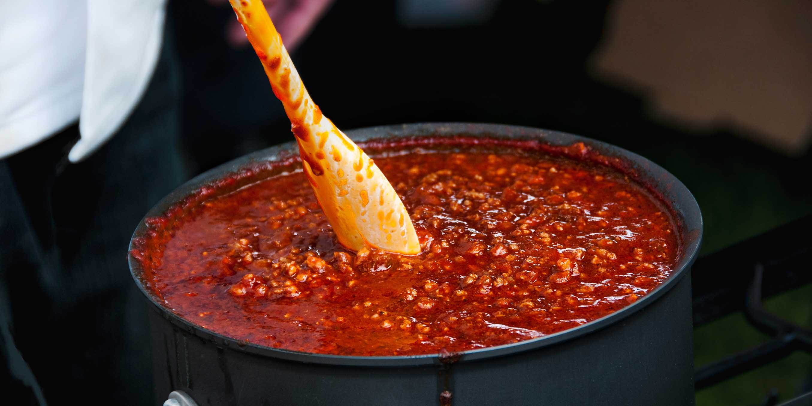 A large pot of ground beef chili being stirred