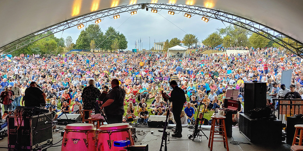 Band playing outside at Richmond Folk Festival with large crowd.