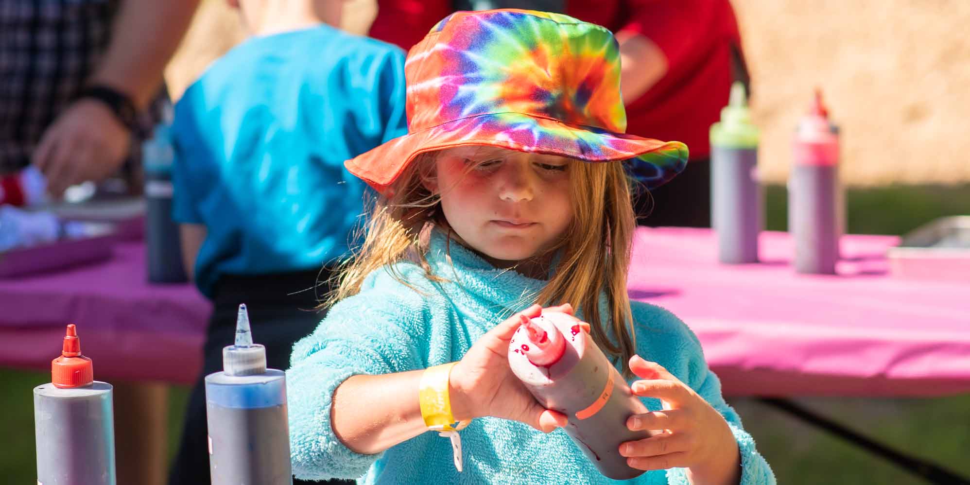 A young girl wearing a tie-dye bucket hat while tie-dying a Camp Fimfo tshirt