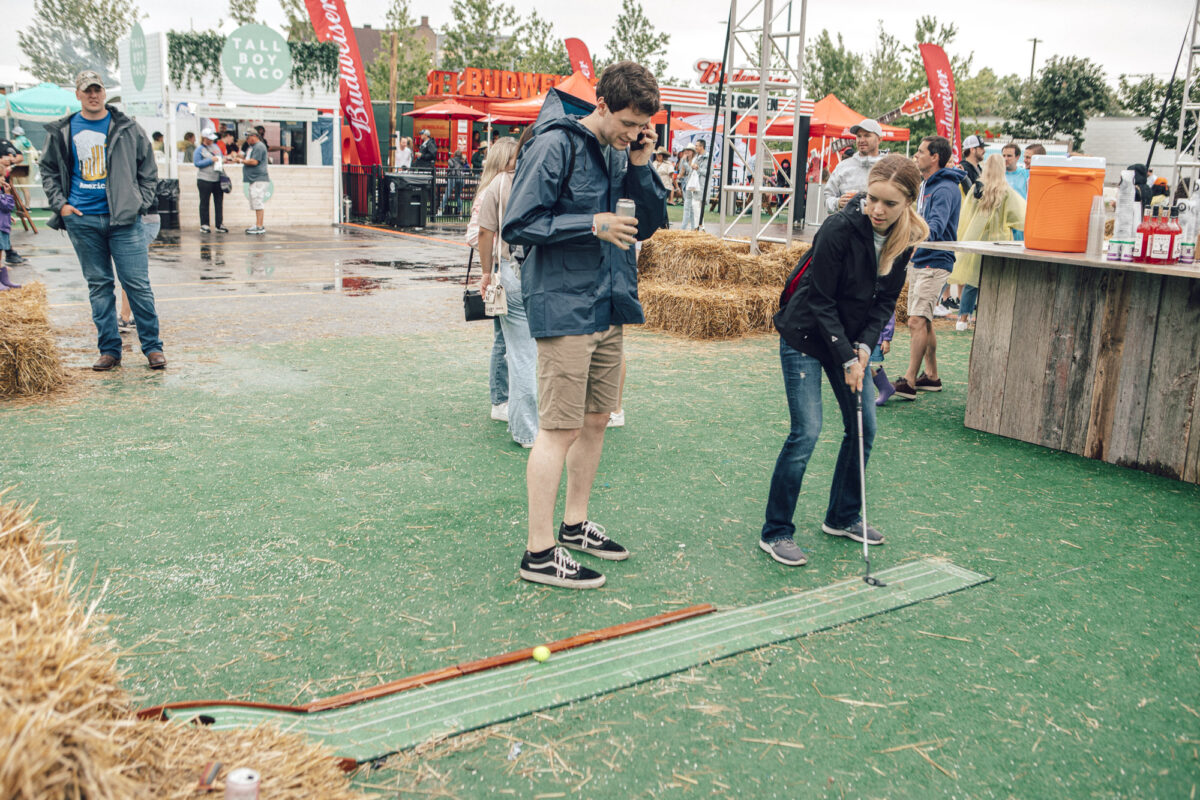 woman lining up a putt on a mini-golf hole with festival food tents in the background