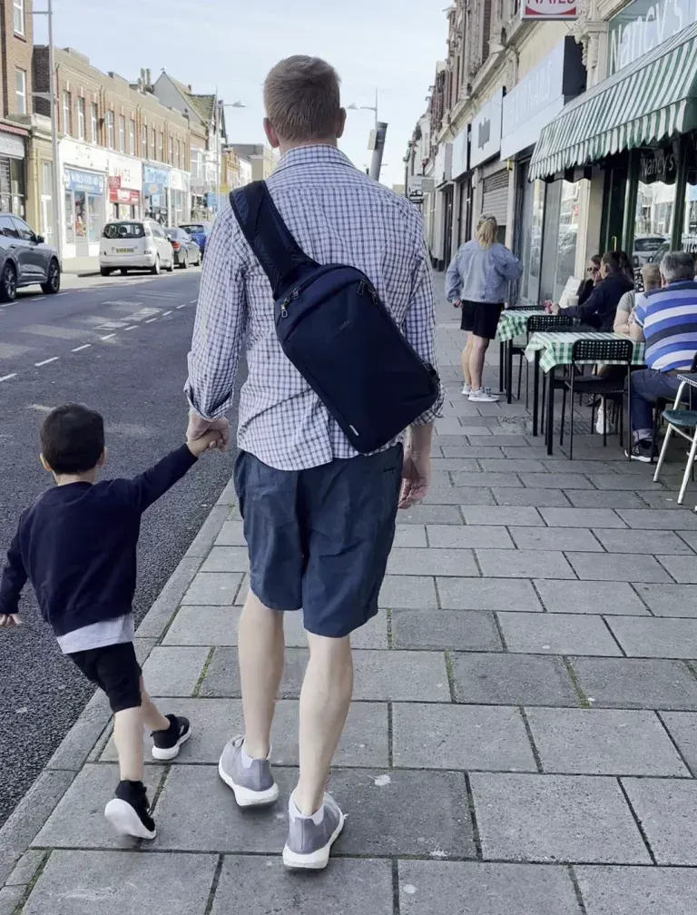 Chris walking down a European street holding Jaxon’s hand, wearing his sling bag