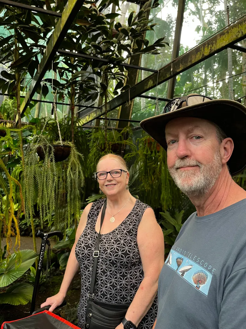 A woman and a man in a bush hat in the glasshouse, among hanging plants