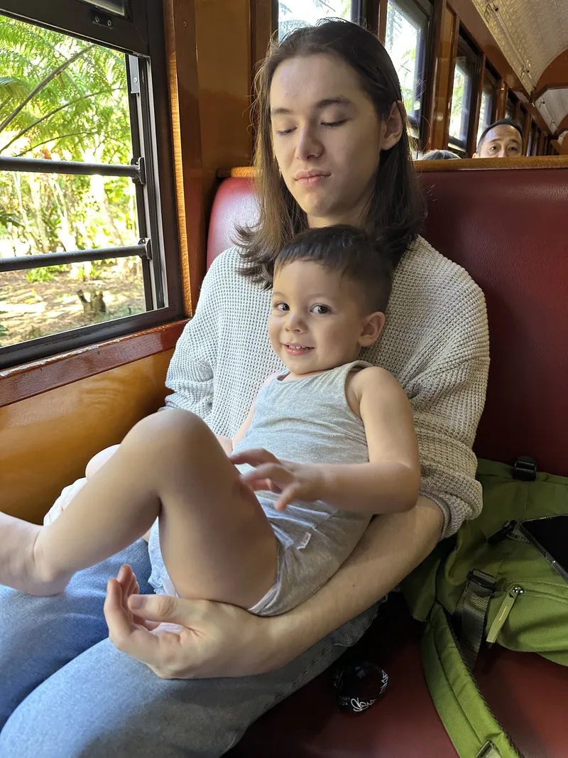 A teenager with a toddler on their lap by the train window