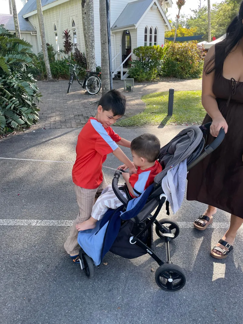 A boy leaning over a toddler in a stroller outside a small white church
