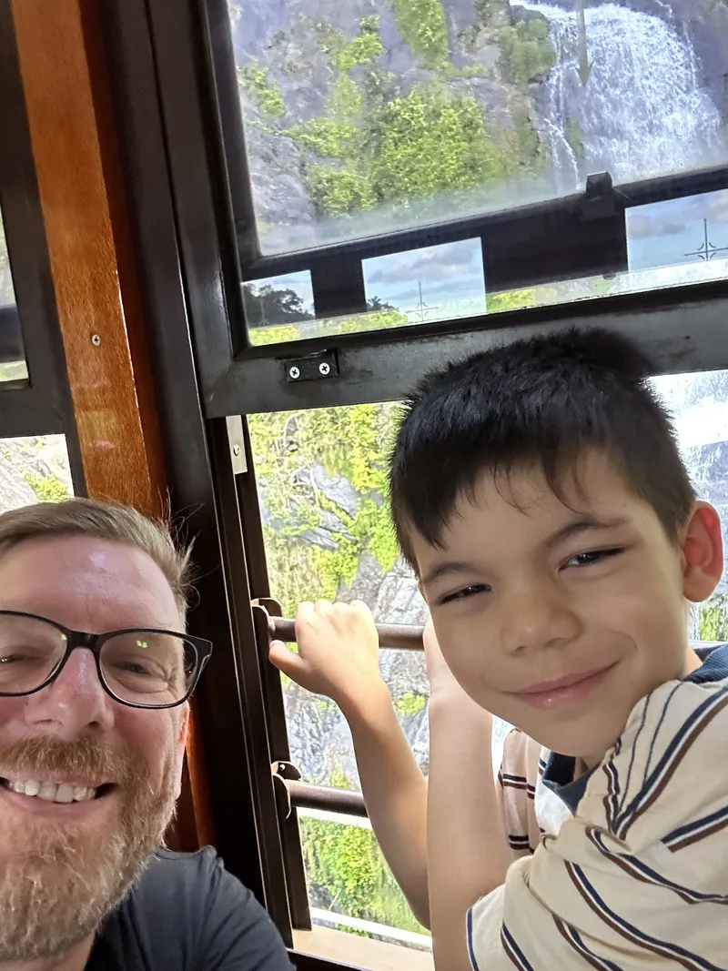 A selfie of a man and a boy at the window by the falls