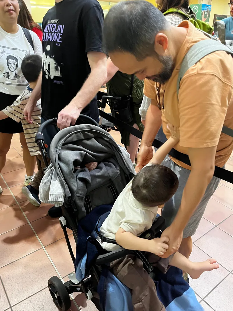 A man helping a toddler into a stroller in the Skyrail queue