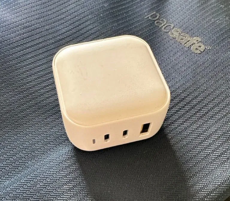 A white multi-port GaN charger on a Pacsafe bag