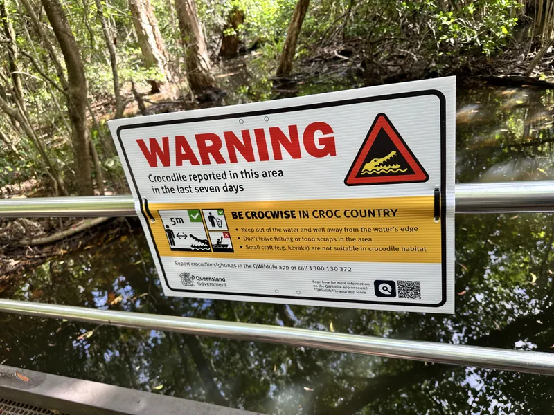 A crocodile warning sign on the railing above a creek