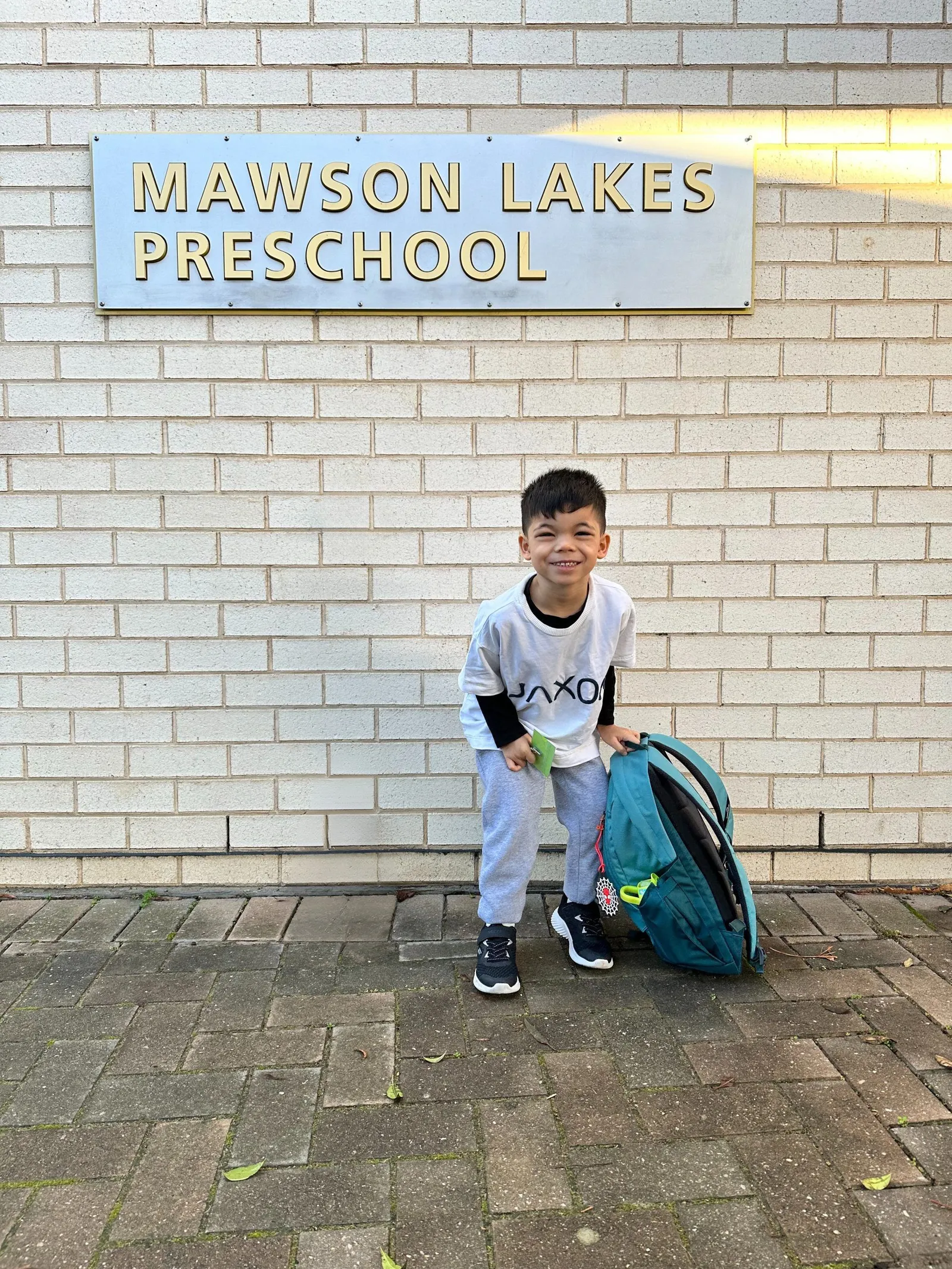 Jaxon smiling with his backpack outside the Mawson Lakes Preschool sign