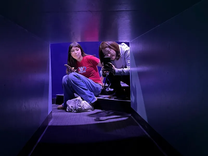 Two people sitting in a dim purple viewing tunnel