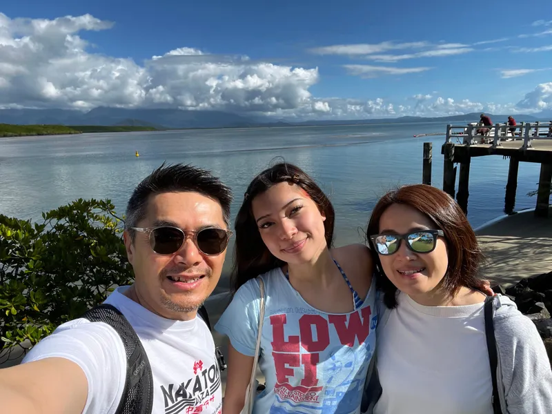 A selfie of three people by the water, with the jetty behind