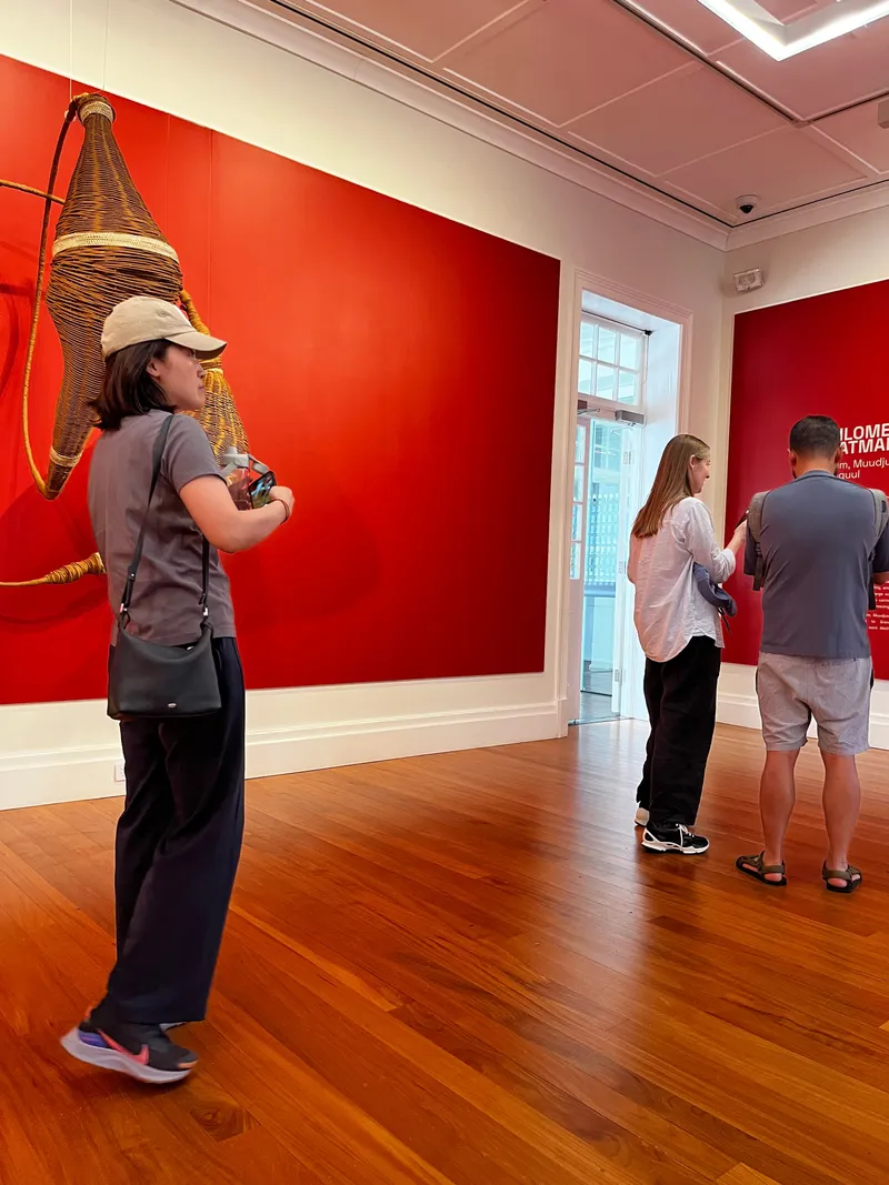 A woman photographing a woven piece hanging on the red wall