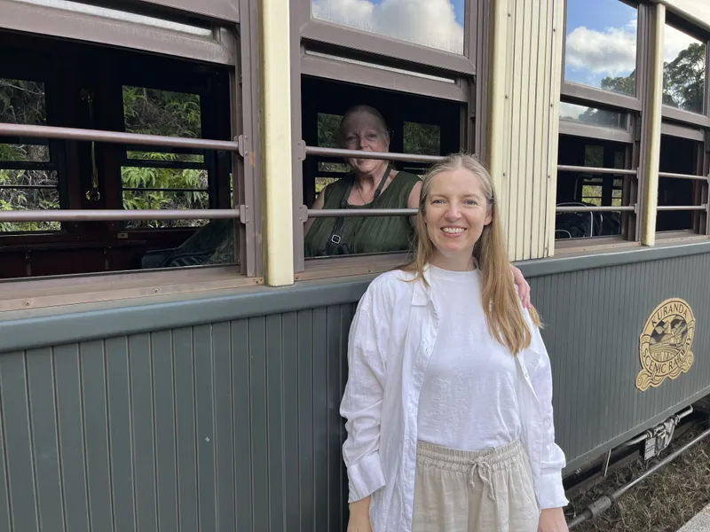 A woman by the train, with an older woman at the window behind her