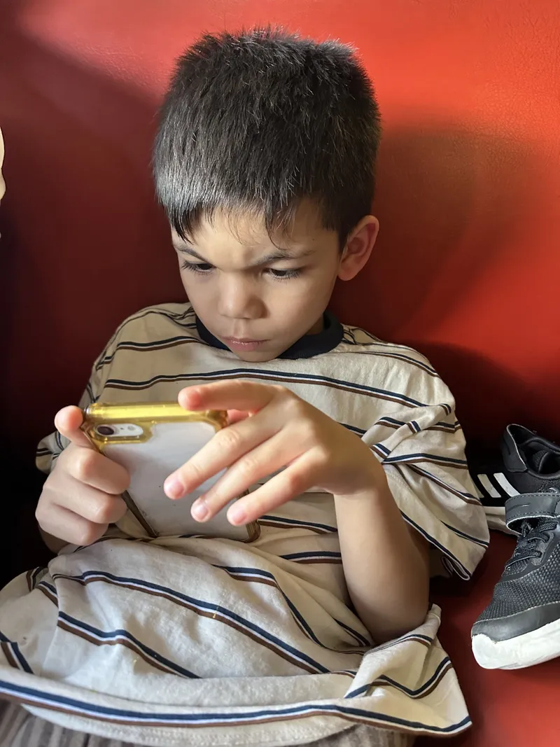 A boy playing on a phone, leaning on the red seat