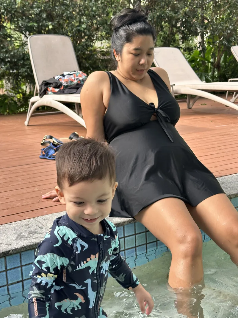 The toddler wading beside the woman sitting on the pool step