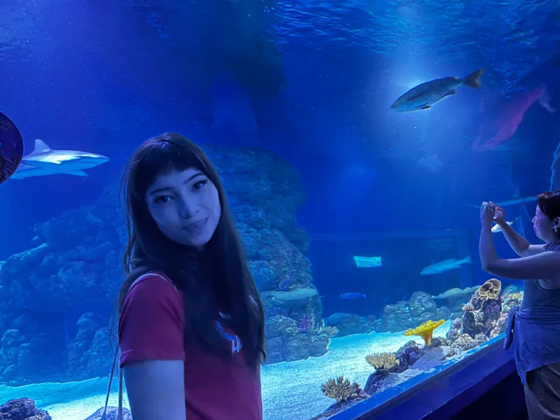 A girl in front of the big tank, with sharks swimming behind