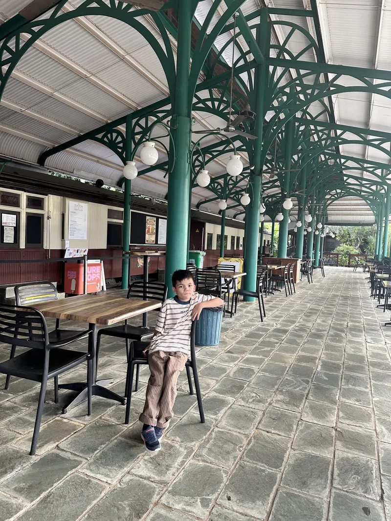 A boy sitting on a cafe chair under the station's green iron roof
