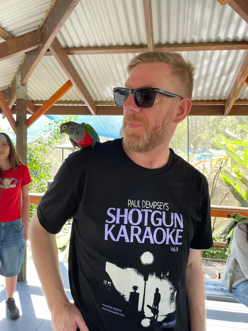 A man in sunglasses with a small parrot on his shoulder