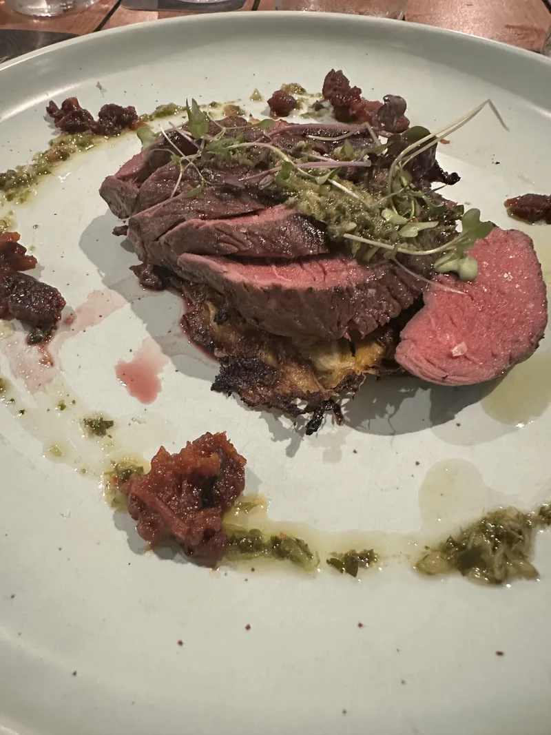 Sliced steak with herbs and sauces on a pale plate