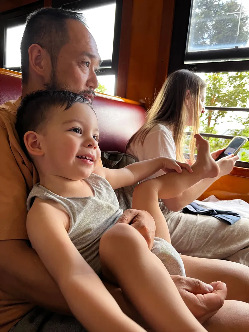 The toddler laughing at the window, with a woman on her phone beside them