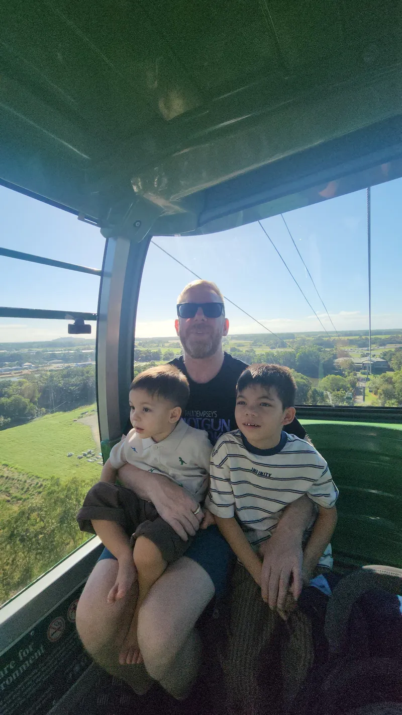 A man with two boys on his lap in a gondola above the canopy