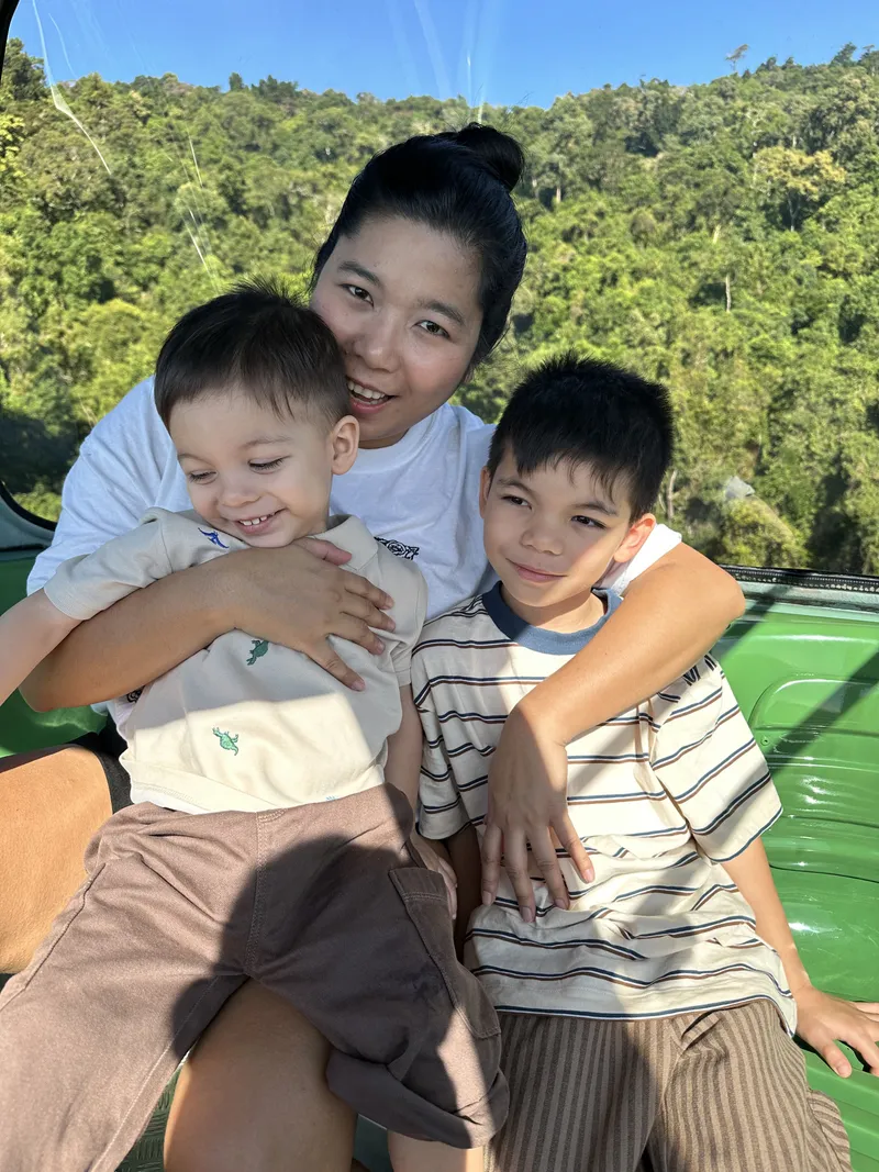 The woman and the two boys laughing in the gondola, the rainforest behind