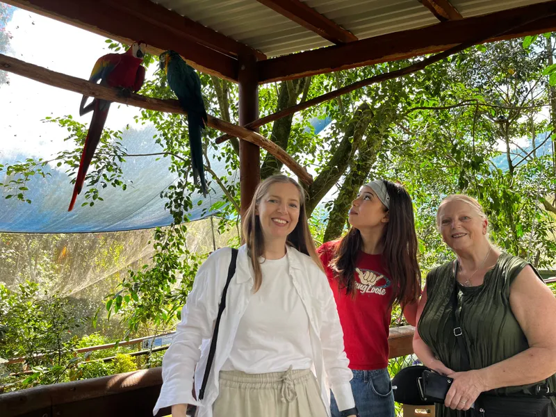 Three women posing beneath a scarlet and a blue-and-gold macaw