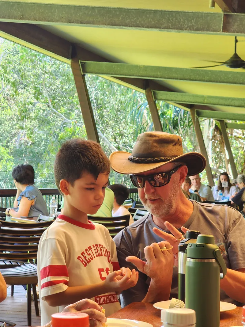 A boy and a man in a bush hat sharing a laugh at the lunch table