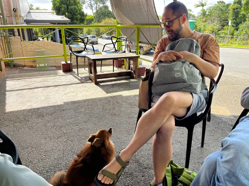 A man sitting outside a cafe with a small dog at his feet