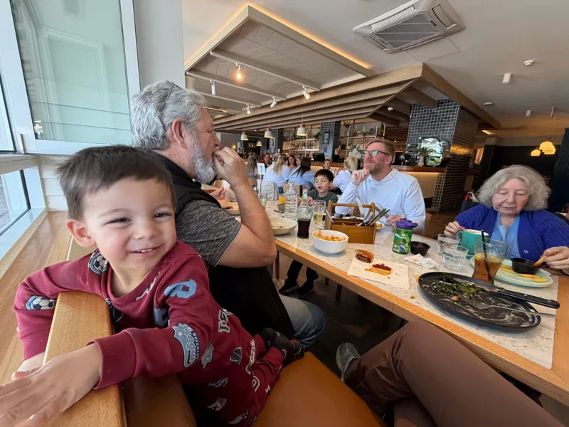 One of the boys grinning at the camera beside the family at a long table