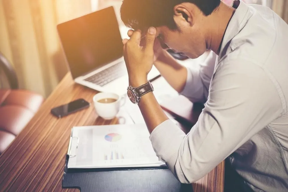 A stressed man with his head in his hands at a laptop