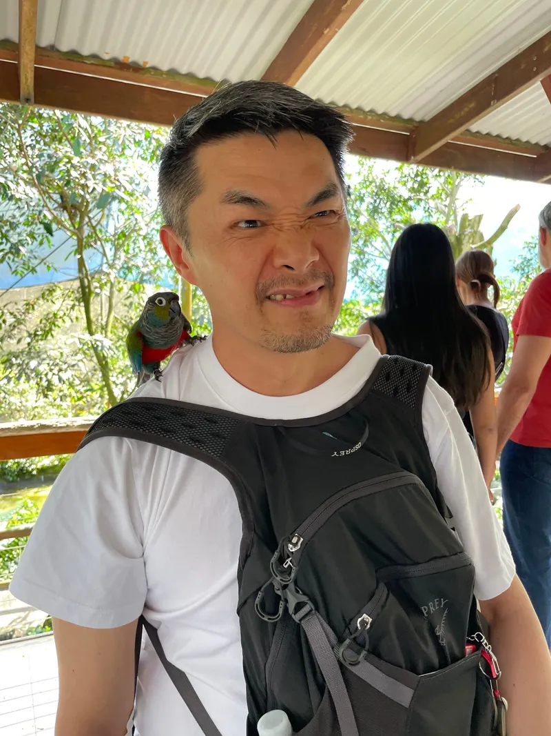 A man pulling a face at the parrot on his shoulder