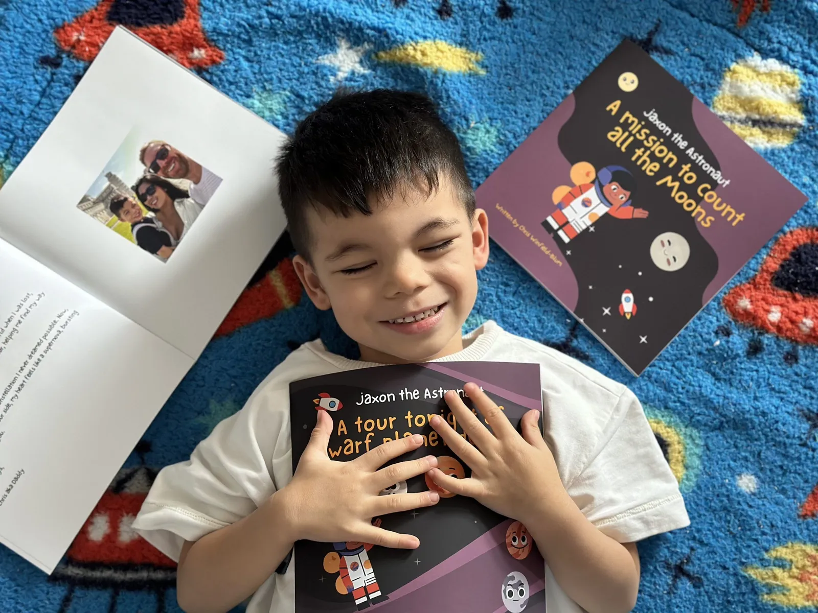 Jaxon lying on a rug hugging a copy of Jaxon the Astronaut, surrounded by the books