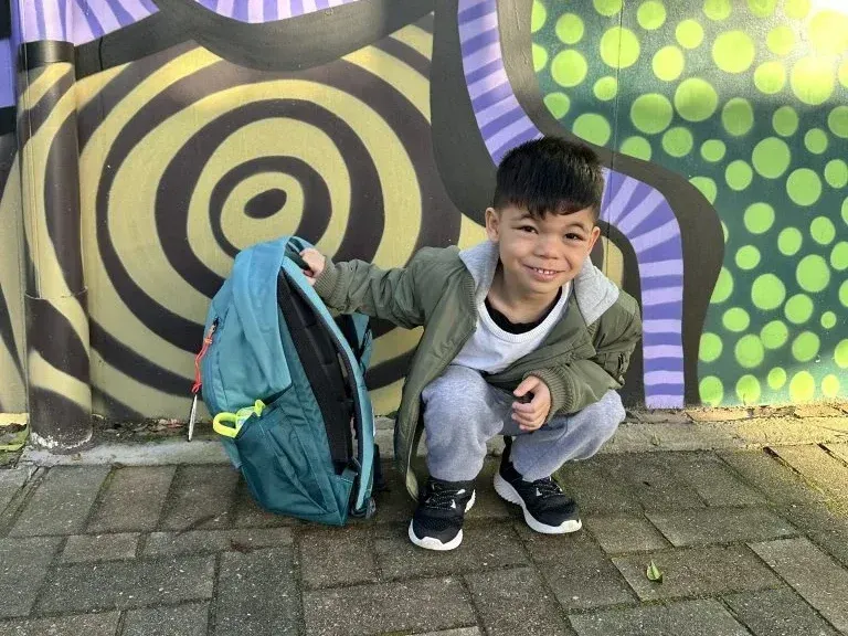 Jaxon crouching with his backpack in front of a colourful painted wall