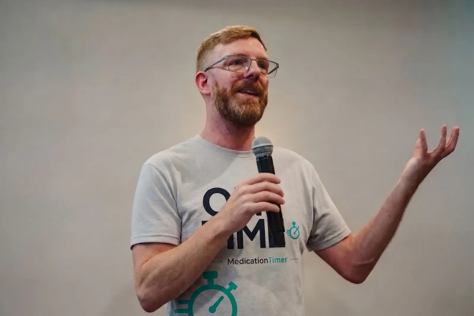 Chris speaking into a microphone in a Medication Timer T-shirt