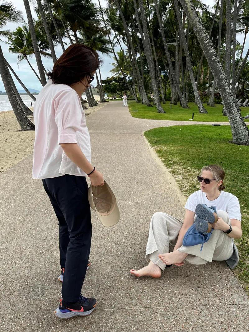 Two people resting on the path under the palms, one sitting on the ground