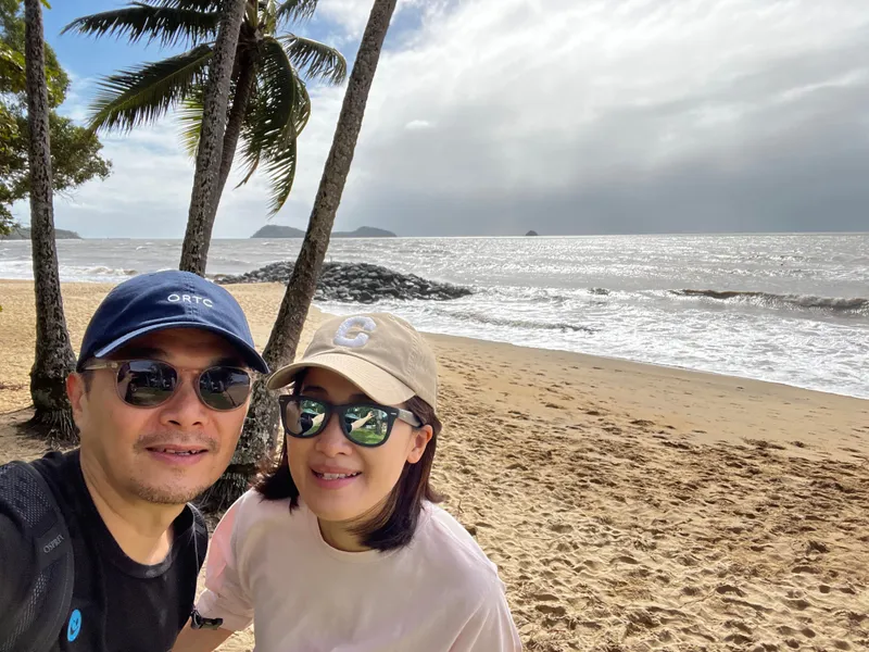 A selfie of two people in caps and sunglasses on the beach