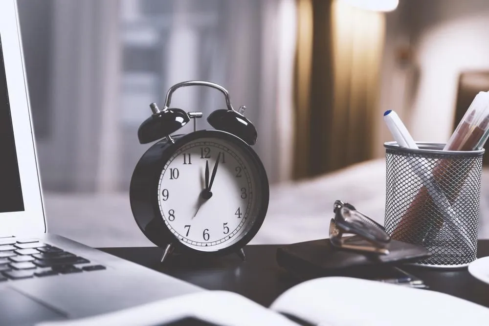 An alarm clock on a desk beside a laptop