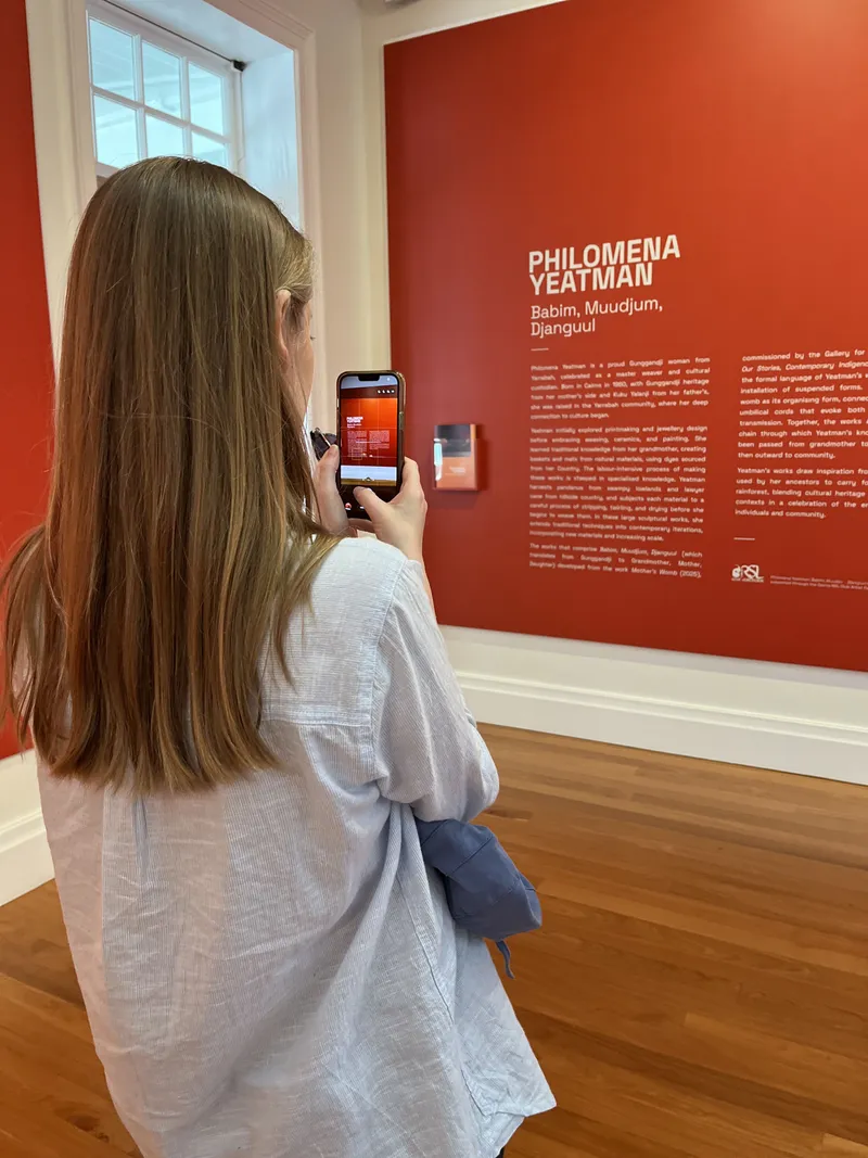A woman photographing the red wall text for the Philomena Yeatman exhibition